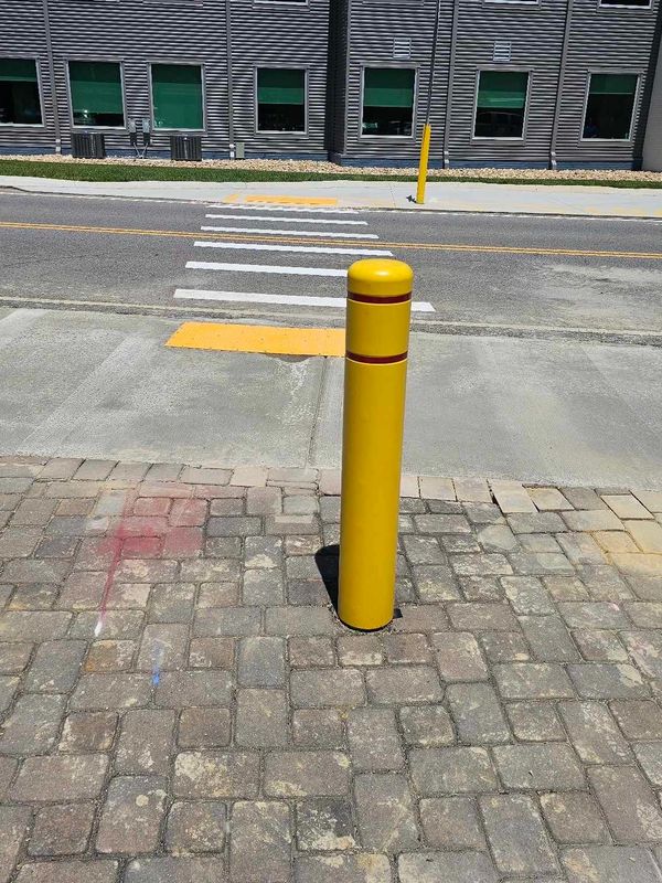 Yellow bollard on a cobblestone sidewalk near a crosswalk and building.