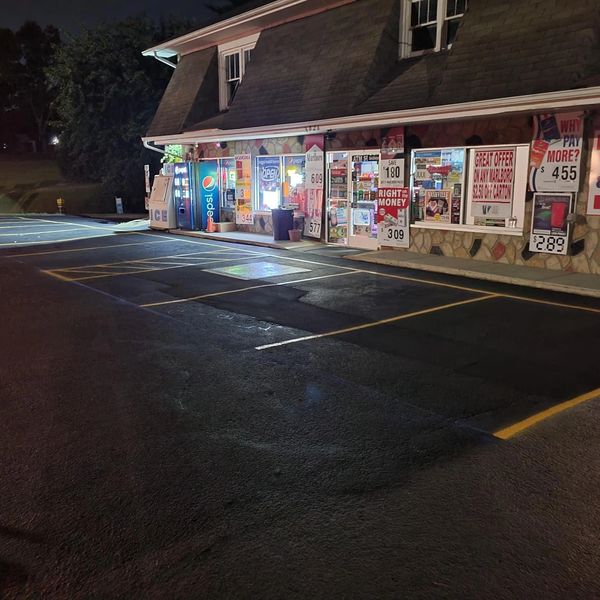 Convenience store at night with illuminated signs and empty parking spaces.