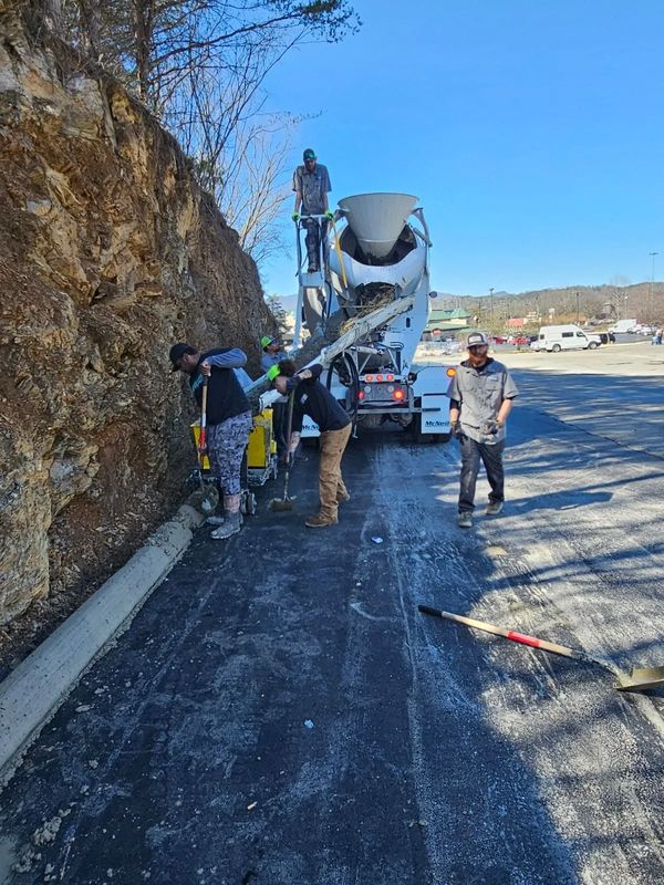 Workers pouring concrete near a rocky hillside with a cement mixer truck.