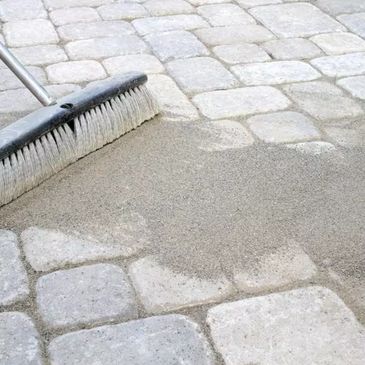 Broom sweeping sand over stone pavement joints.