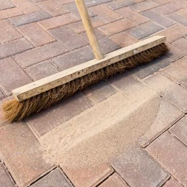 A broom cleaning sand off a brick pavement.