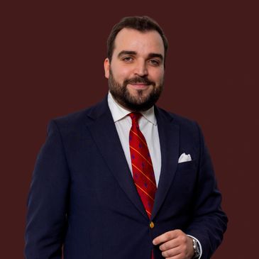 Confident man in a navy suit with a red striped tie against a dark background.