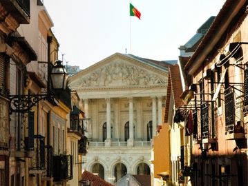 Historic building with Portuguese flag atop, seen through a narrow street.