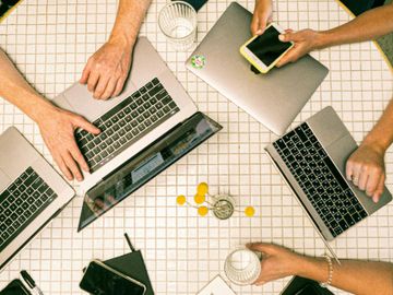 Overhead view of people working with laptops and a smartphone at a round table.