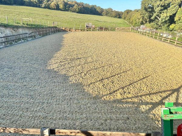 Empty fenced riding arena with shadows on sandy ground.