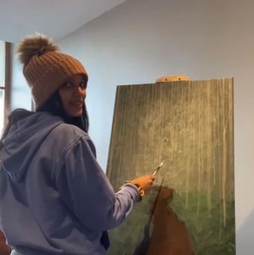 A woman in a brown beanie painting on a canvas indoors.