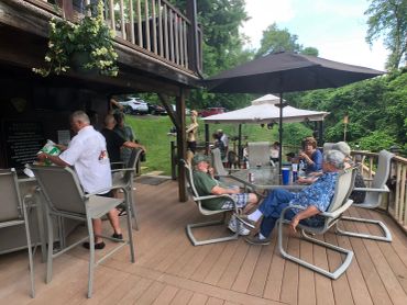 People relaxing on a wooden deck with umbrellas and greenery.