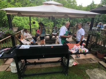 People enjoying a backyard barbecue under a canopy with a large grill.