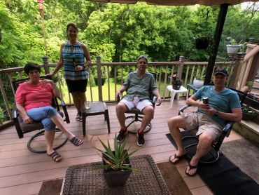 Four people relaxing on a wooden deck surrounded by greenery.