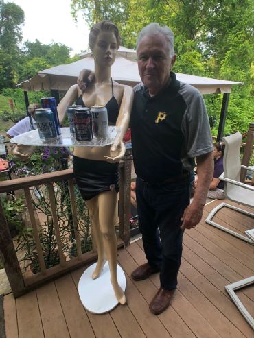 Man standing next to a mannequin holding a tray with drinks on a wooden deck.