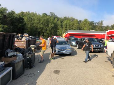 People loading electronics into vehicles in a parking lot.