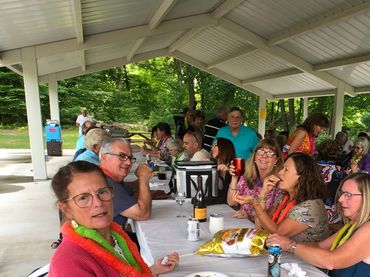 Group of people enjoying a picnic under a pavilion with colorful leis.