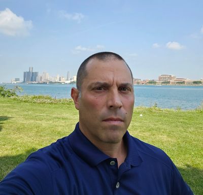 Man taking selfie near a waterfront with city skyline in background.