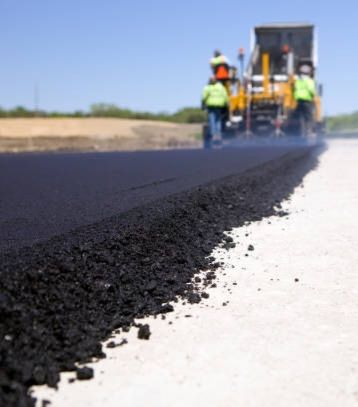 Workers paving a road with fresh asphalt on a sunny day.