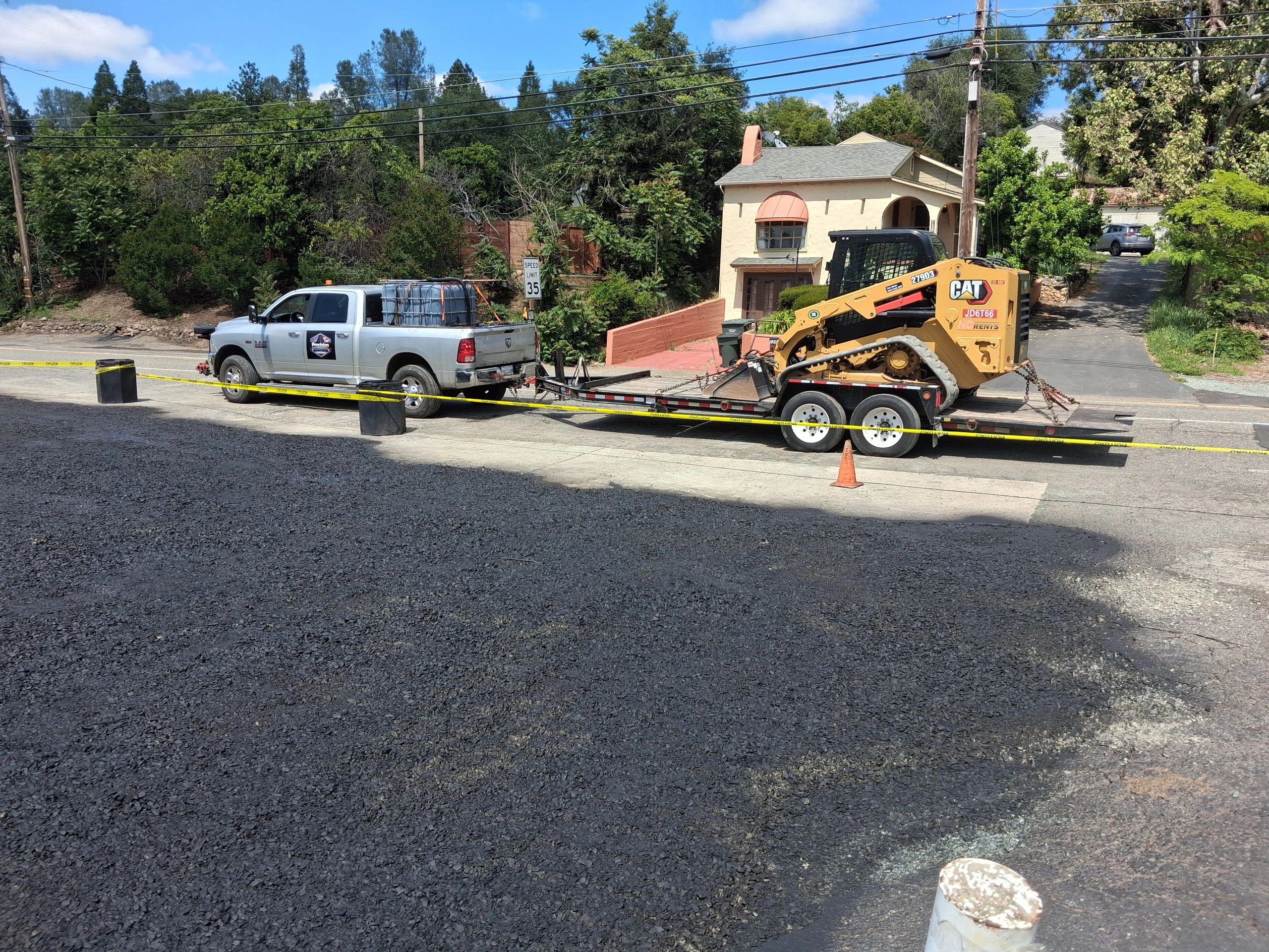 Pickup truck towing a construction vehicle on a trailer during roadwork.