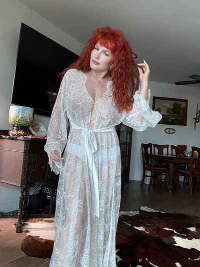 Woman with red curly hair in a white lace robe in a cozy living room.