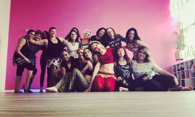 A group of women posing happily in a dance studio with a pink wall.