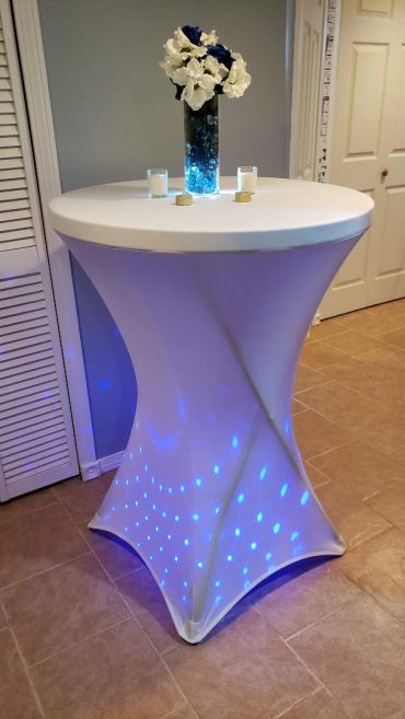 Tall table with white cloth and blue lights, decorated with flowers and candles.