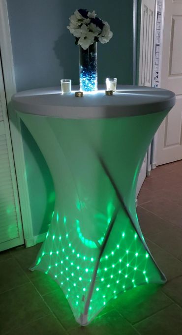 Illuminated tall table with white flowers and candles.