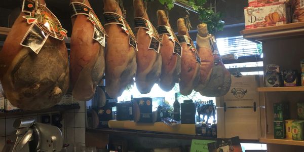 Cured hams hanging in a rustic deli or kitchen setting.