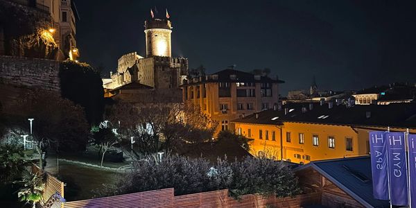Night view of an illuminated castle tower and surrounding buildings.