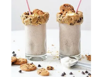 Two tall glasses filled with a creamy, frothy milkshake topped with a cookie and whipped cream.

