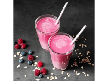 Two glasses of pink smoothie with rolled oats, raspberries, and blueberries scattered around them.

