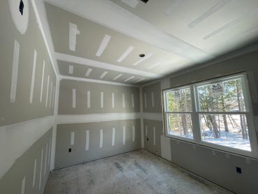 A room under construction with drywall installed and taped, sunlight coming through the window.