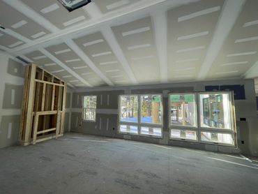 An unfinished room with drywall and large windows letting in natural light.