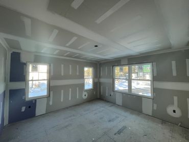 A room under construction with drywall installed and windows letting in natural light.