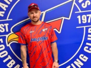Man in a red Falcons sports jersey standing before a blue team logo backdrop.