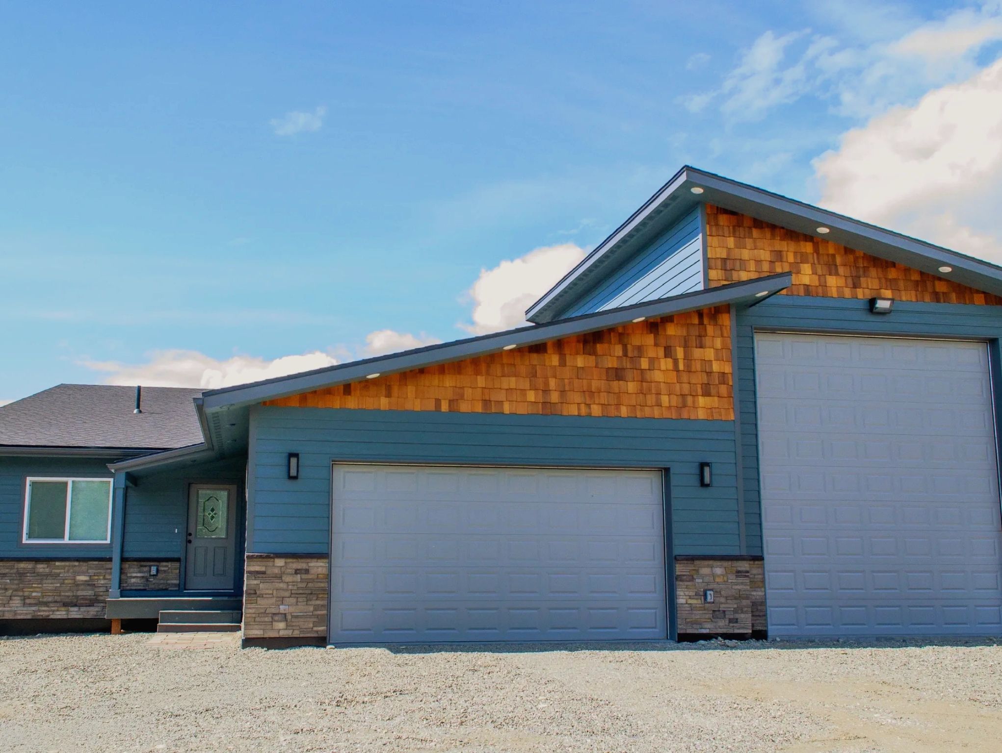 Modern blue house with wooden accents and a spacious garage under a bright sky.
