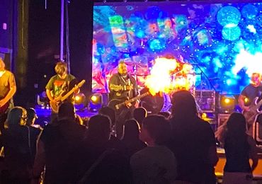 Band performing live with vibrant light effects and pyrotechnics.