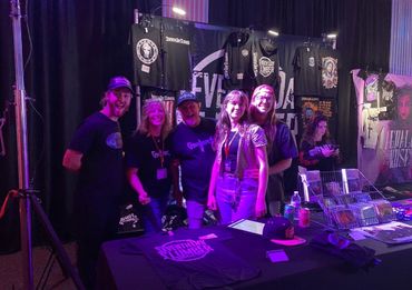 Group of five people smiling at a merchandise booth with band t-shirts.