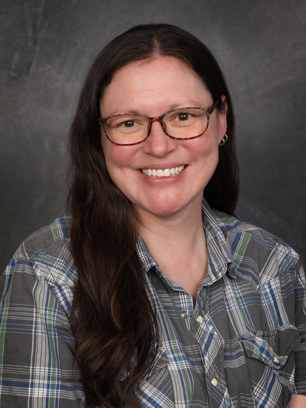 Smiling woman with long brown hair and glasses, wearing a plaid shirt.