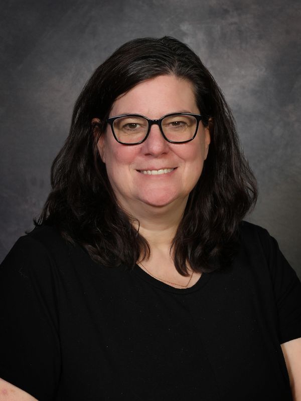 Smiling woman with glasses and dark hair against a gray backdrop.