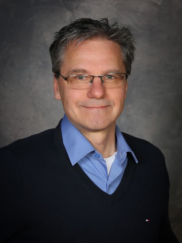 Professional portrait of a middle-aged man with glasses and a friendly smile.