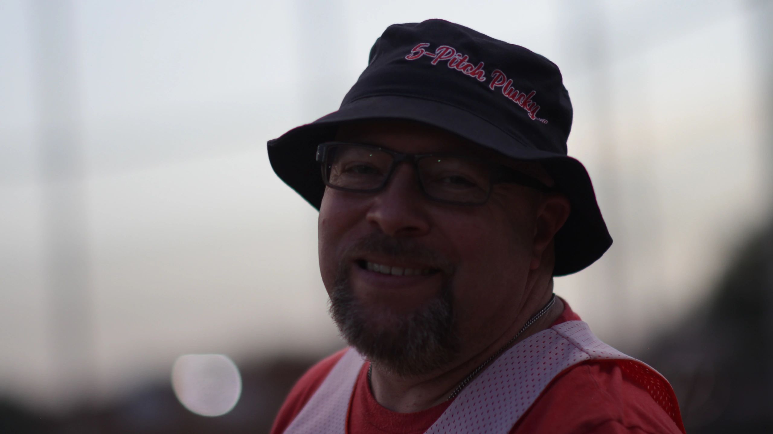 A man with a 5-Pitch Plucky® bucket hat on smiling because he's having a blast playing baseball.