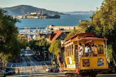 A classic San Francisco cable car descending a hill with Alcatraz Island in the background.
