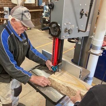 Elderly man using a bandsaw to cut wood.