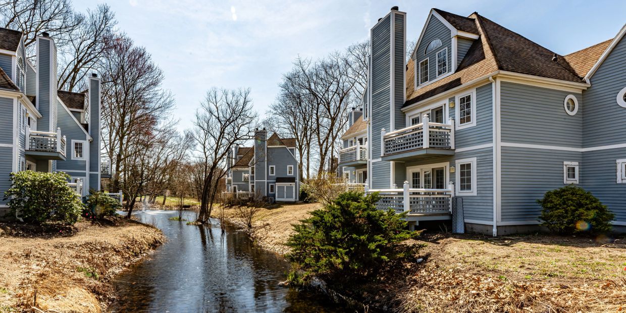 Blue houses with balconies beside a narrow water canal and leafless trees.