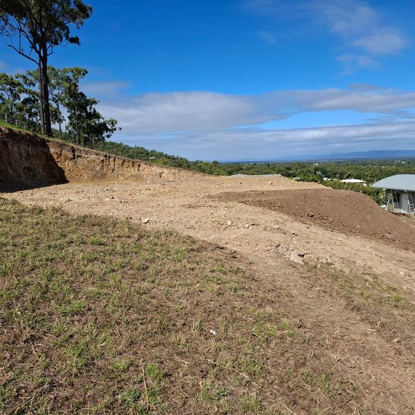 Cleared dirt land on a hill with trees and blue sky in the background.