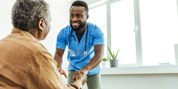 Smiling healthcare worker holds hands with elderly patient.