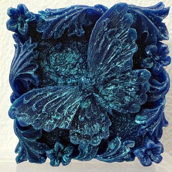 Intricately carved blue butterfly with floral accents on a square base.