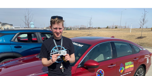 A boy standing in front of a red car