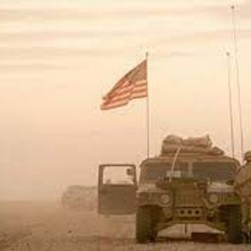Military vehicle with American flag in a dusty desert environment.