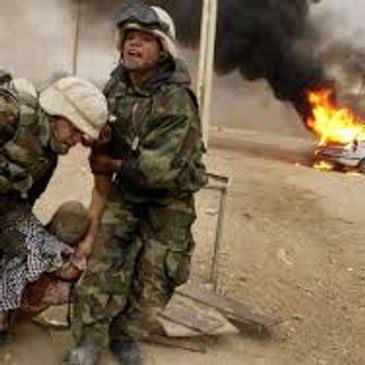 Soldiers rescuing an injured person near a burning vehicle.