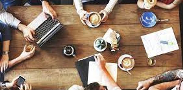Group meeting over coffee and laptops at a wooden table.
