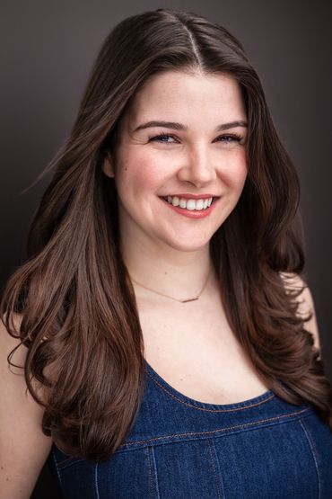 Smiling woman with long brown hair wearing a denim top.
