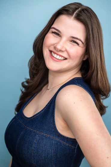 Smiling woman in a denim dress against a light blue background.
